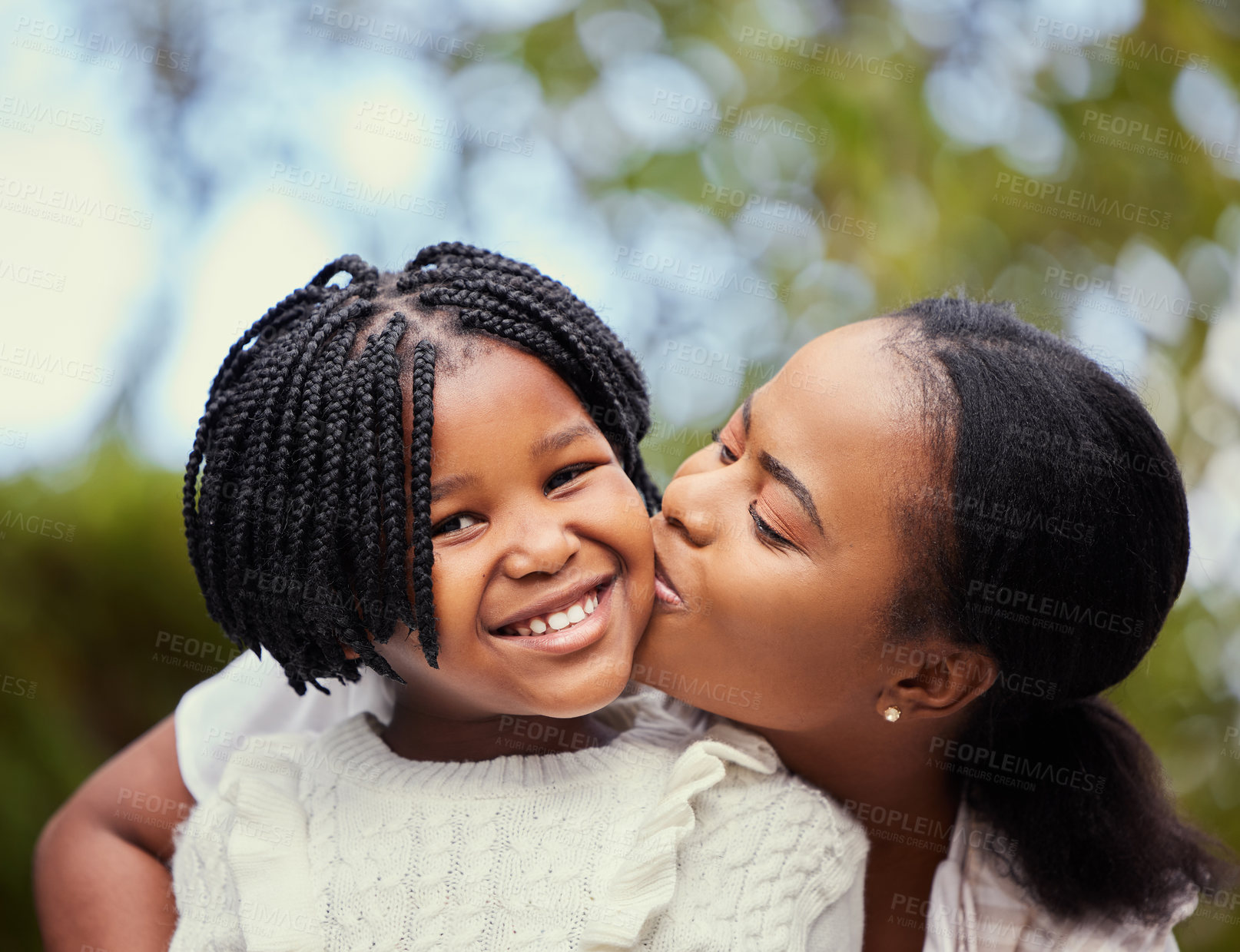 Buy stock photo Shot of a young mother giving her daughter a kiss in nature