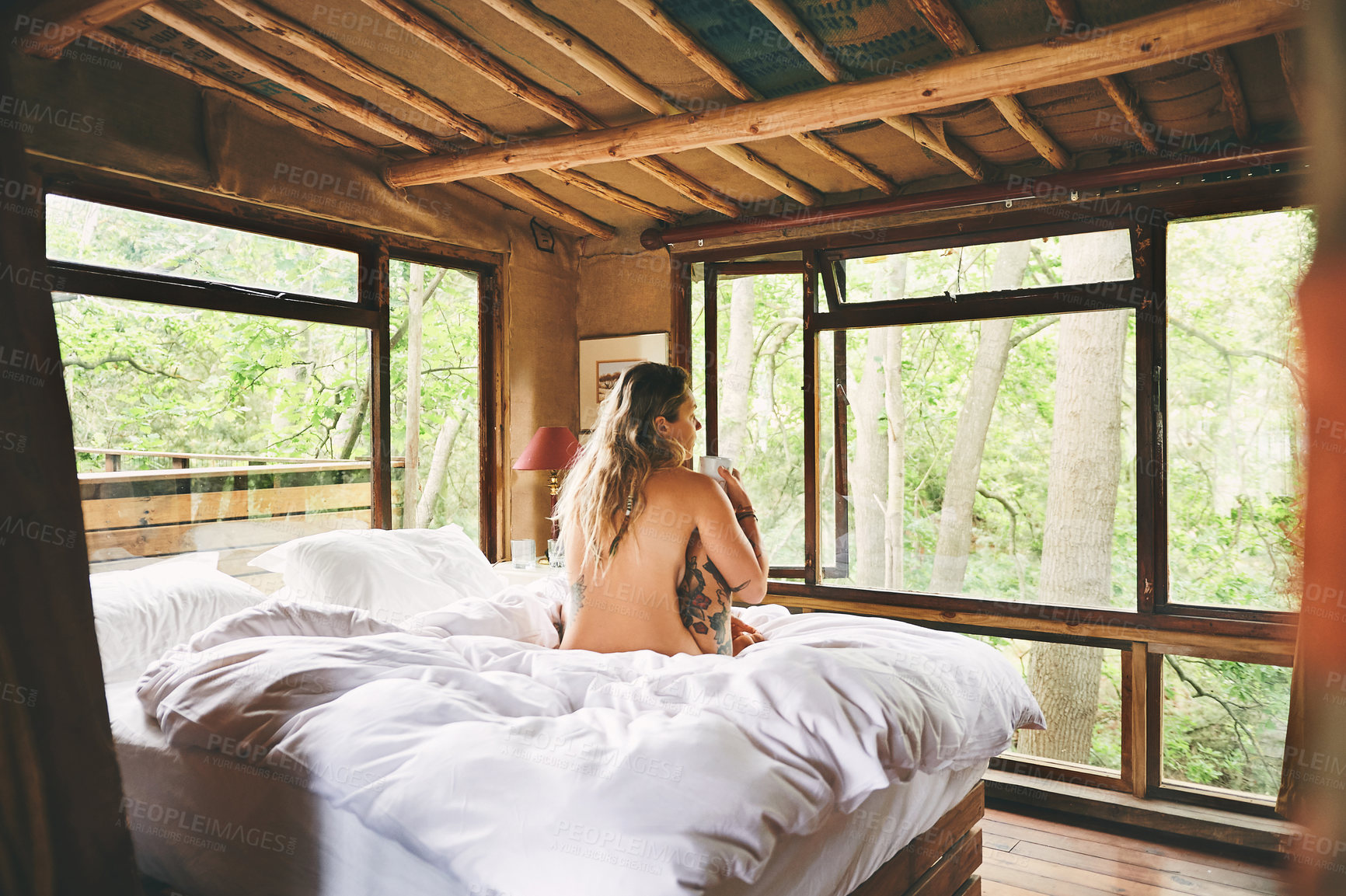 Buy stock photo Rearview shot of a woman sitting naked on a bed in a cabin