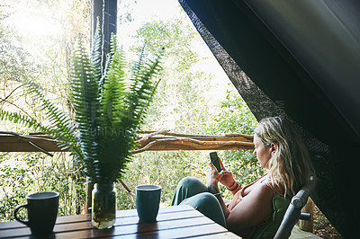 Buy stock photo Shot of a young woman using her cellphone while relaxing on a porch at a cabin