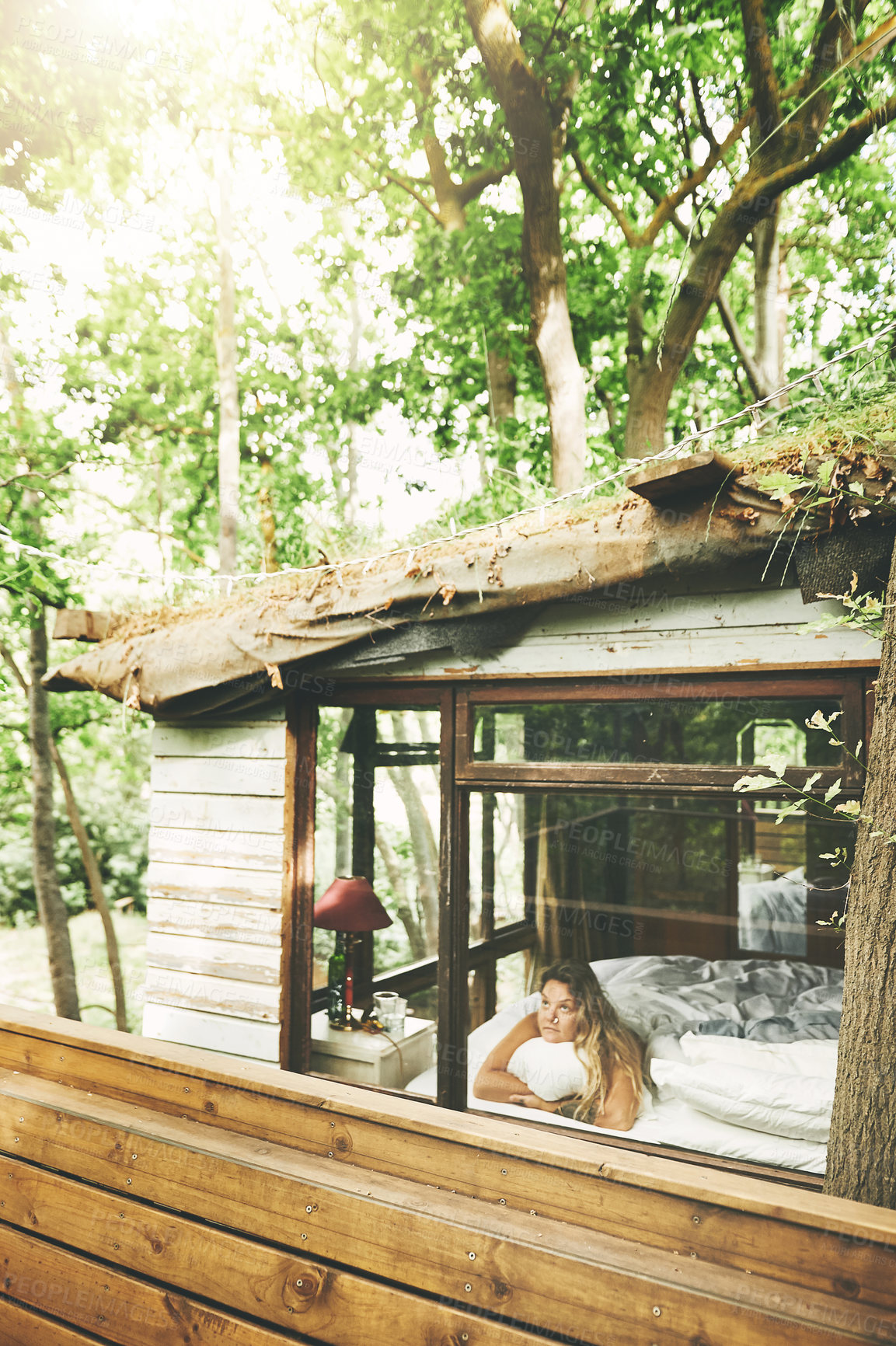 Buy stock photo Shot of a young woman looking out the window while lying on a bed in a cabin