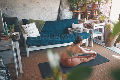 Buy stock photo Shot of a young woman touching her toes while exercising at home