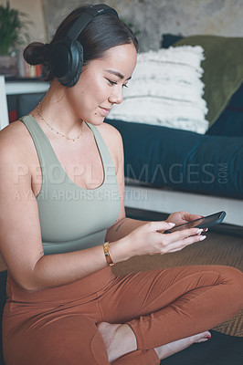 Buy stock photo Shot of a young woman wearing headphones and using a cellphone while exercising at home