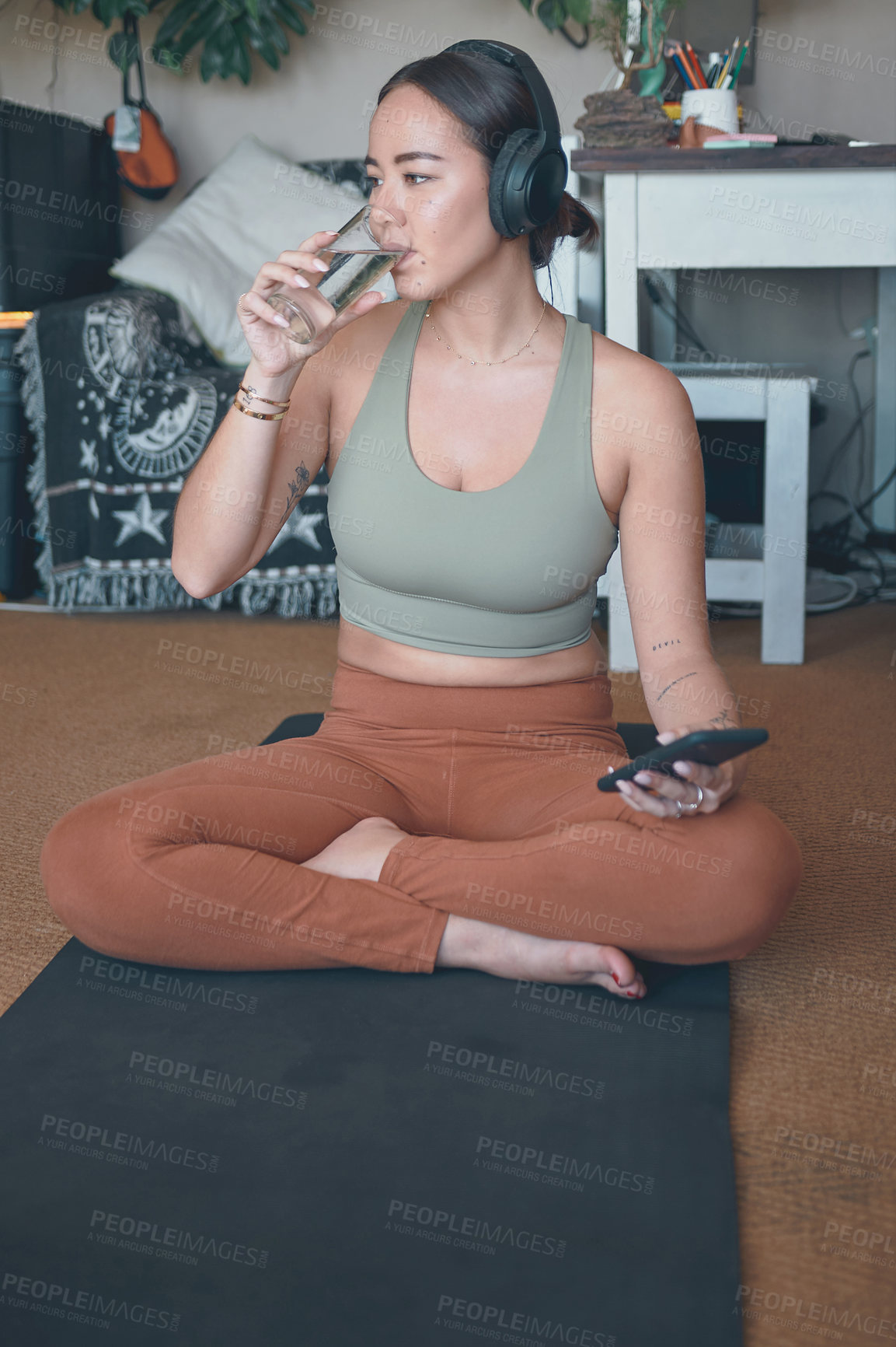 Buy stock photo Shot of a young woman drinking water and using a cellphone while exercising at home