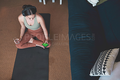 Buy stock photo High angle shot of a young woman wearing headphones and using a cellphone while exercising at home