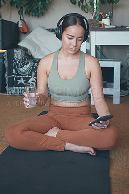 Buy stock photo Shot of a young woman wearing headphones and using a cellphone while exercising at home