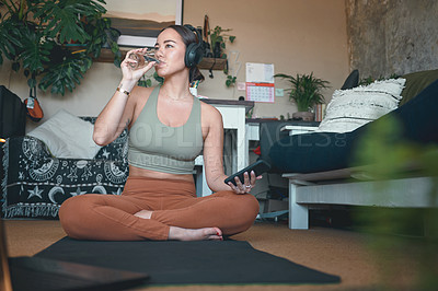 Buy stock photo Shot of a young woman drinking water and using a cellphone while exercising at home