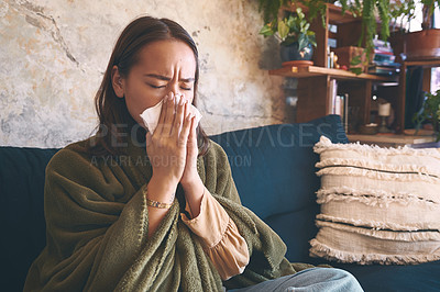 Buy stock photo Shot of a young woman blowing her nose while recovering from an illness on the sofa at home