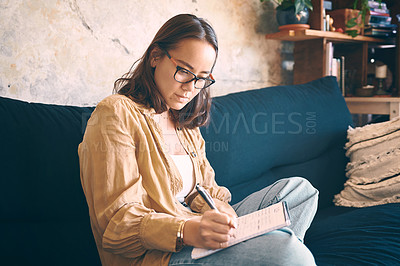 Buy stock photo Shot  of a young woman making notes while relaxing on the sofa at home