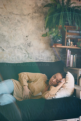 Buy stock photo Shot of a young woman experiencing stomach pain while lying on the sofa at home