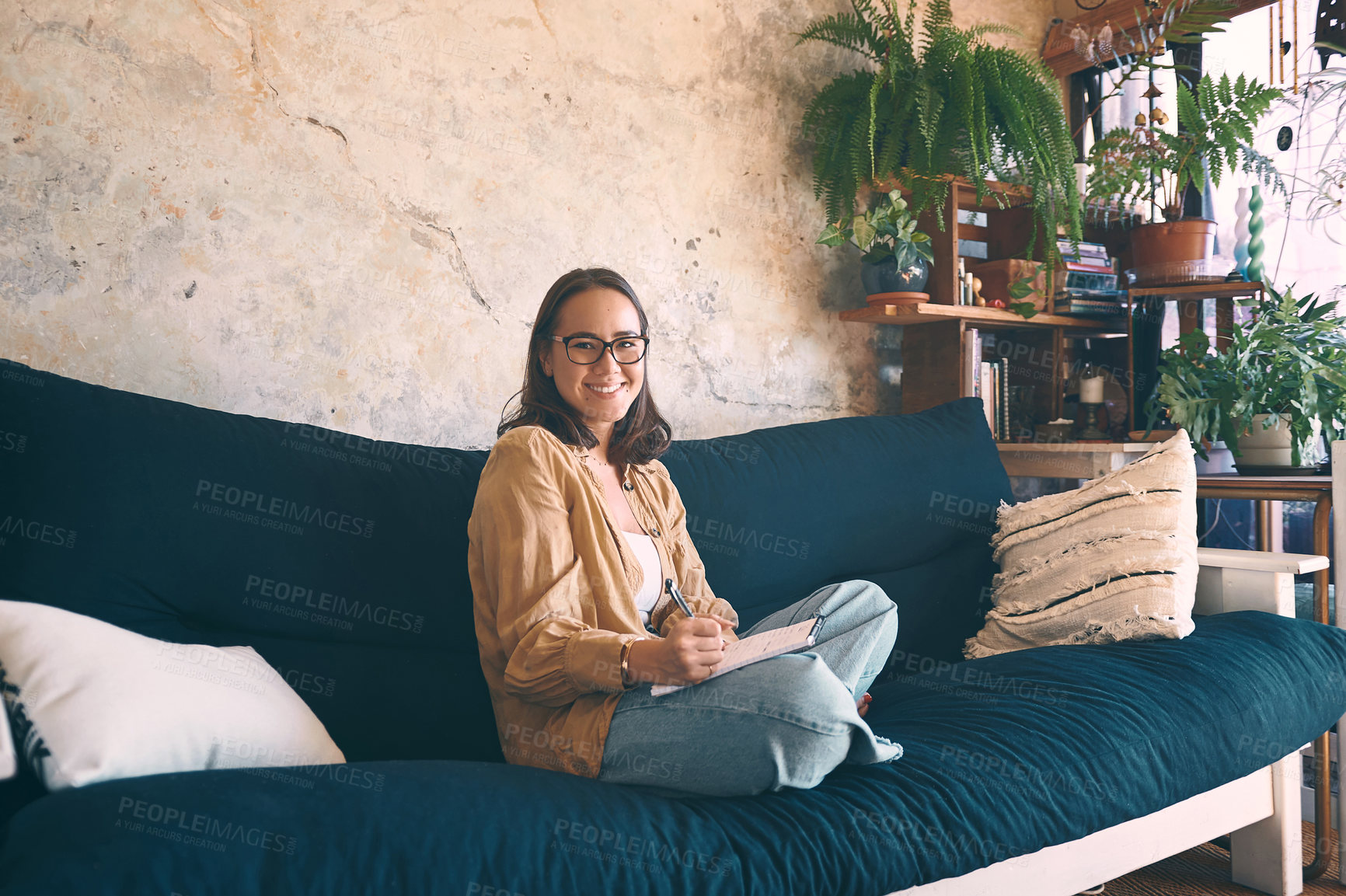 Buy stock photo Shot  of a young woman making notes while relaxing on the sofa at home