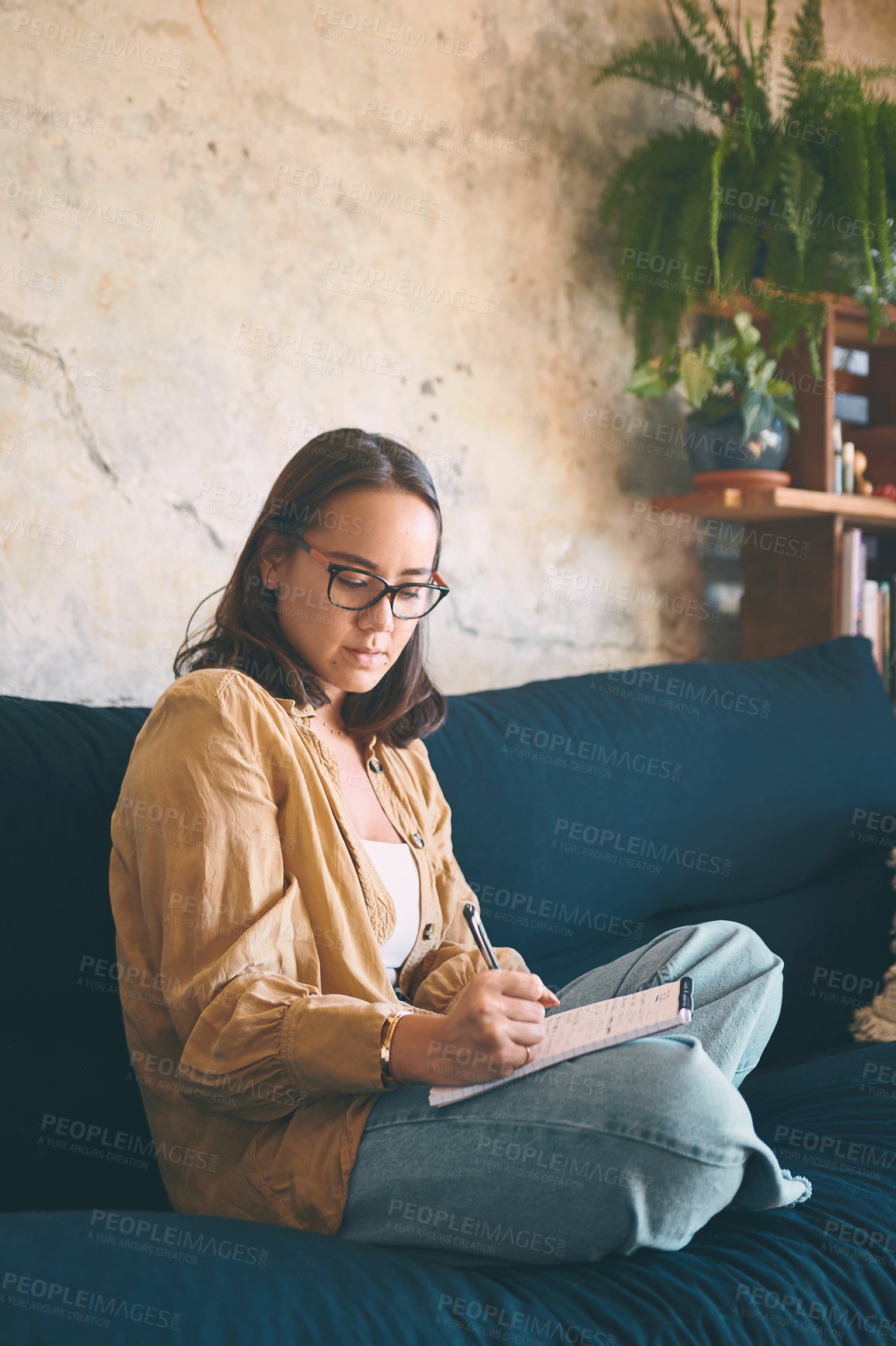 Buy stock photo Shot  of a young woman making notes while relaxing on the sofa at home