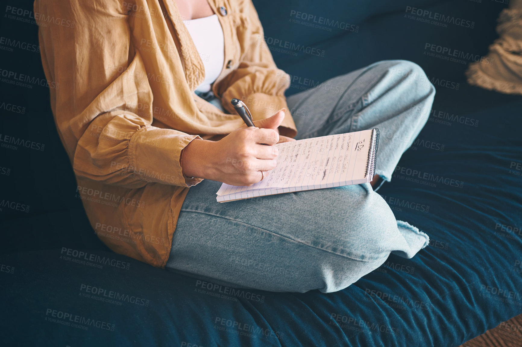 Buy stock photo Shot of an unrecognisable woman making notes while relaxing on the sofa at home