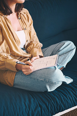 Buy stock photo Shot of an unrecognisable woman making notes while relaxing on the sofa at home