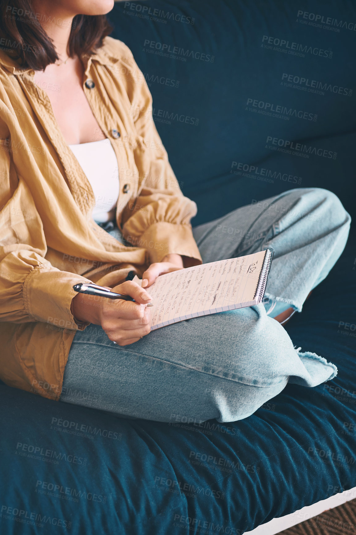 Buy stock photo Shot of an unrecognisable woman making notes while relaxing on the sofa at home