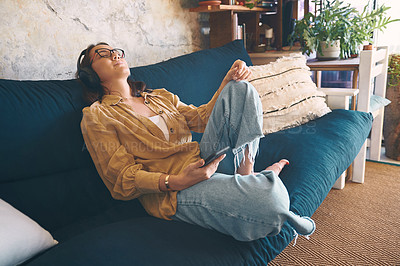 Buy stock photo Shot of a young woman using headphones and a smartphone while relaxing on the sofa at home