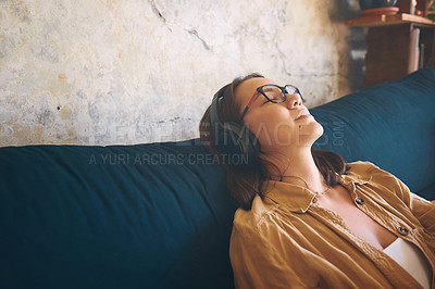 Buy stock photo Shot of a young woman using headphones while relaxing on the sofa at home