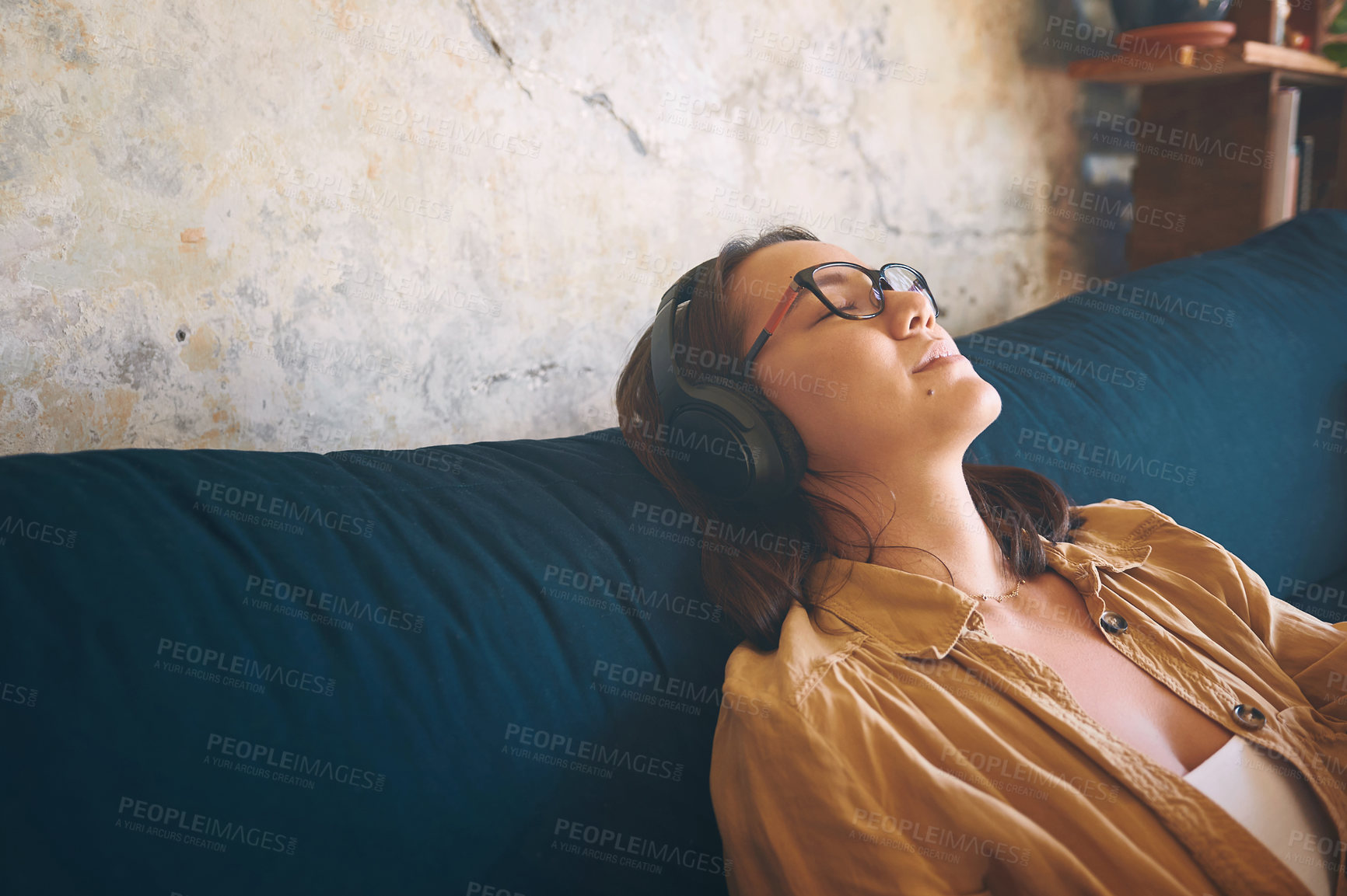 Buy stock photo Shot of a young woman using headphones while relaxing on the sofa at home