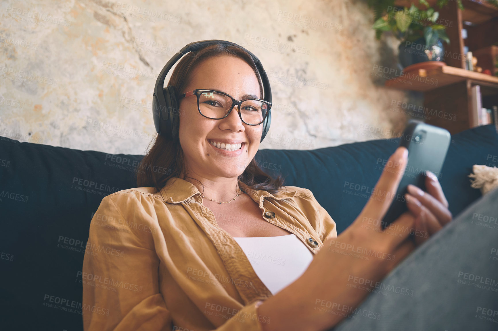 Buy stock photo Shot of a young woman using headphones and a smartphone while relaxing on the sofa at home