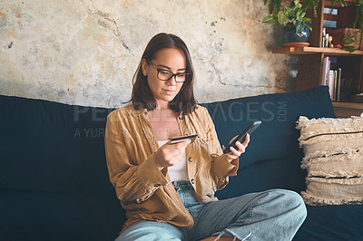 Buy stock photo Shot of a young woman using a smartphone and credit card on the sofa at home