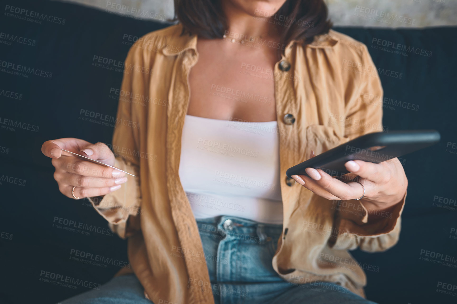 Buy stock photo Shot of an unrecognisable woman using a smartphone and credit card on the sofa at home