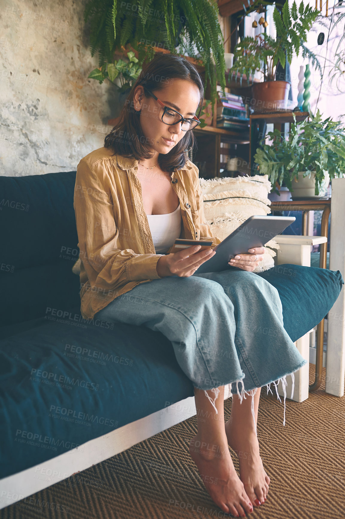 Buy stock photo Shot of a young woman using a digital tablet and credit card on the sofa at home