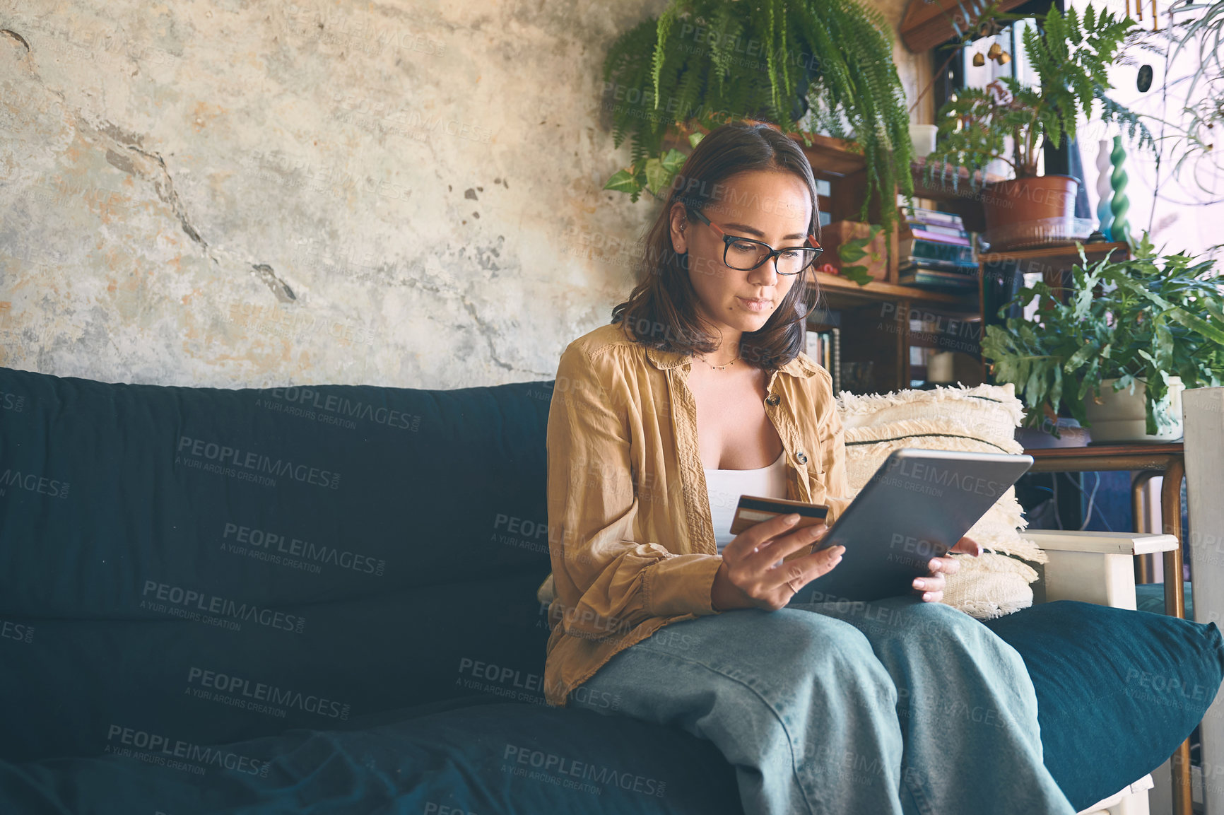 Buy stock photo Shot of a young woman using a digital tablet and credit card on the sofa at home