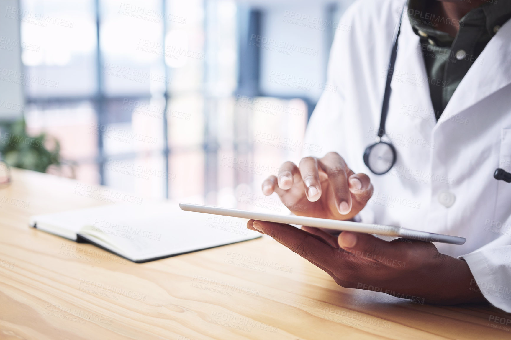 Buy stock photo Cropped shot of an unrecognizable doctor sitting alone in his office at the clinic and using his digital tablet