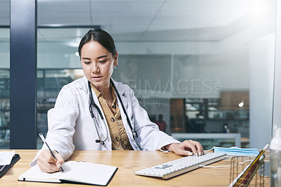 Buy stock photo Shot of an attractive young doctor sitting alone in her office at the clinic and writing in her notebook