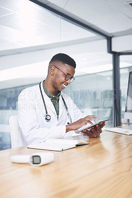 Buy stock photo Shot of a handsome young doctor sitting alone in his office at the clinic and using his digital tablet