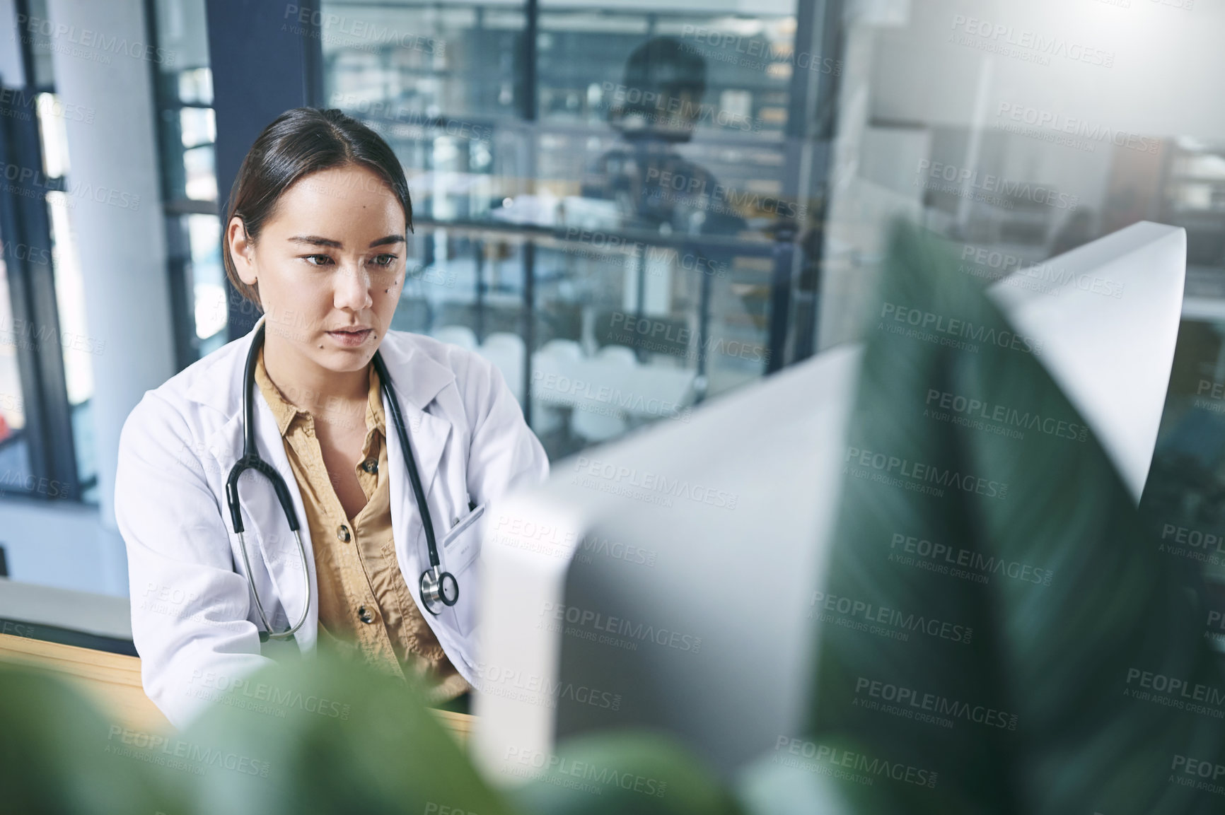 Buy stock photo Shot of an attractive young doctor sitting alone in her office at the clinic and using her computer