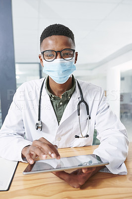 Buy stock photo Shot of a young doctor wearing a face mask and sitting in his office at the clinic while using technology