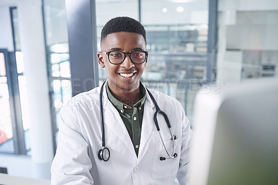 Buy stock photo Shot of a handsome young doctor sitting alone in his office at the clinic and using his computer