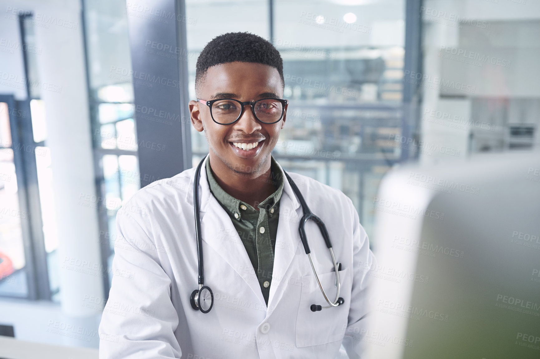 Buy stock photo Shot of a handsome young doctor sitting alone in his office at the clinic and using his computer