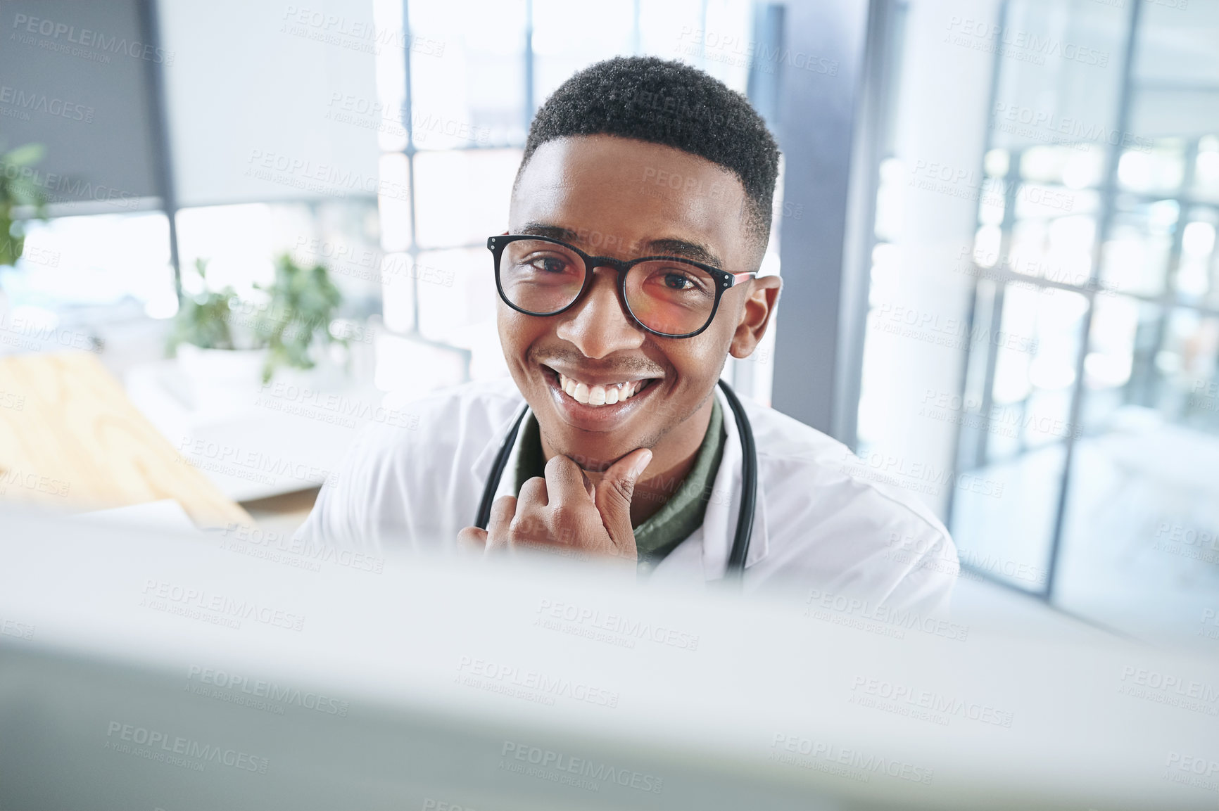 Buy stock photo Shot of a handsome young doctor sitting alone in his office at the clinic and using his computer