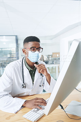 Buy stock photo Shot of a young doctor wearing a mask and sitting in his office at the clinic while using a computer