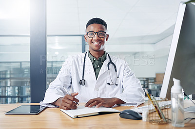 Buy stock photo Shot of a handsome young doctor sitting alone in his office at the clinic and writing in his notebook