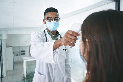 Buy stock photo Shot of a young doctor wearing a mask and standing with a patient in the clinic while taking her temperature