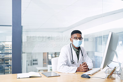 Buy stock photo Shot of a young doctor wearing a face mask and sitting at his desk in his office at the clinic