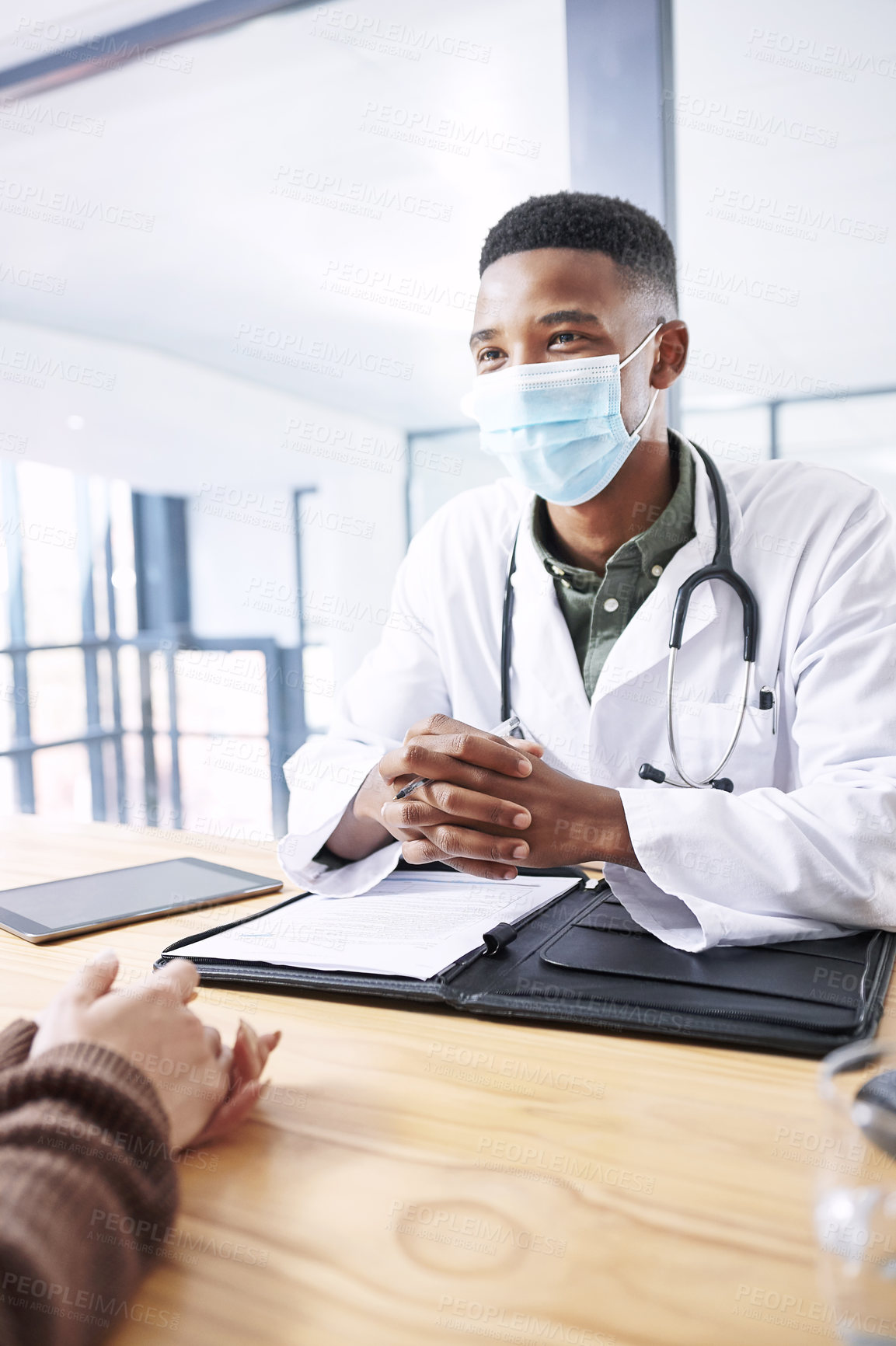 Buy stock photo Shot of a young doctor sitting with his patient and wearing his face mask during a consultation in the clinic