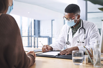 Buy stock photo Shot of a young doctor sitting with his patient and wearing a mask while writing a prescription during a consultation