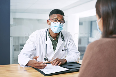 Buy stock photo Shot of a young doctor sitting with his patient and wearing his face mask during a consultation in the clinic