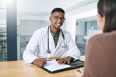 Buy stock photo Shot of a handsome young doctor sitting with his patient and writing a prescription during a consultation in the clinic