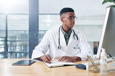 Buy stock photo Shot of a handsome young doctor sitting alone in his office at the clinic and writing in his notebook