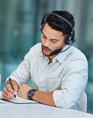 Buy stock photo Shot of a young businessman making notes while working in a call center