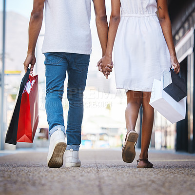 Buy stock photo Shot of a young couple walking hand in hand while holding shopping bags