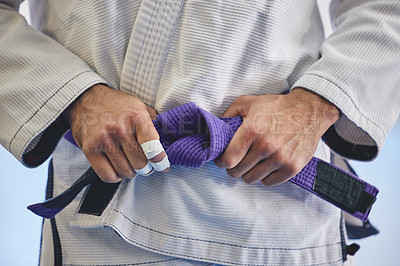 Buy stock photo Cropped shot of an unrecognizable man tying a purple belt around hist waist while in full jiu jitsu gi