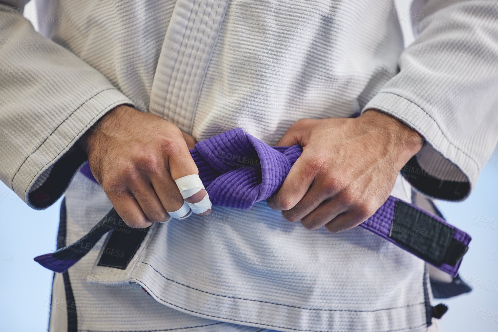 Buy stock photo Cropped shot of an unrecognizable man tying a purple belt around hist waist while in full jiu jitsu gi