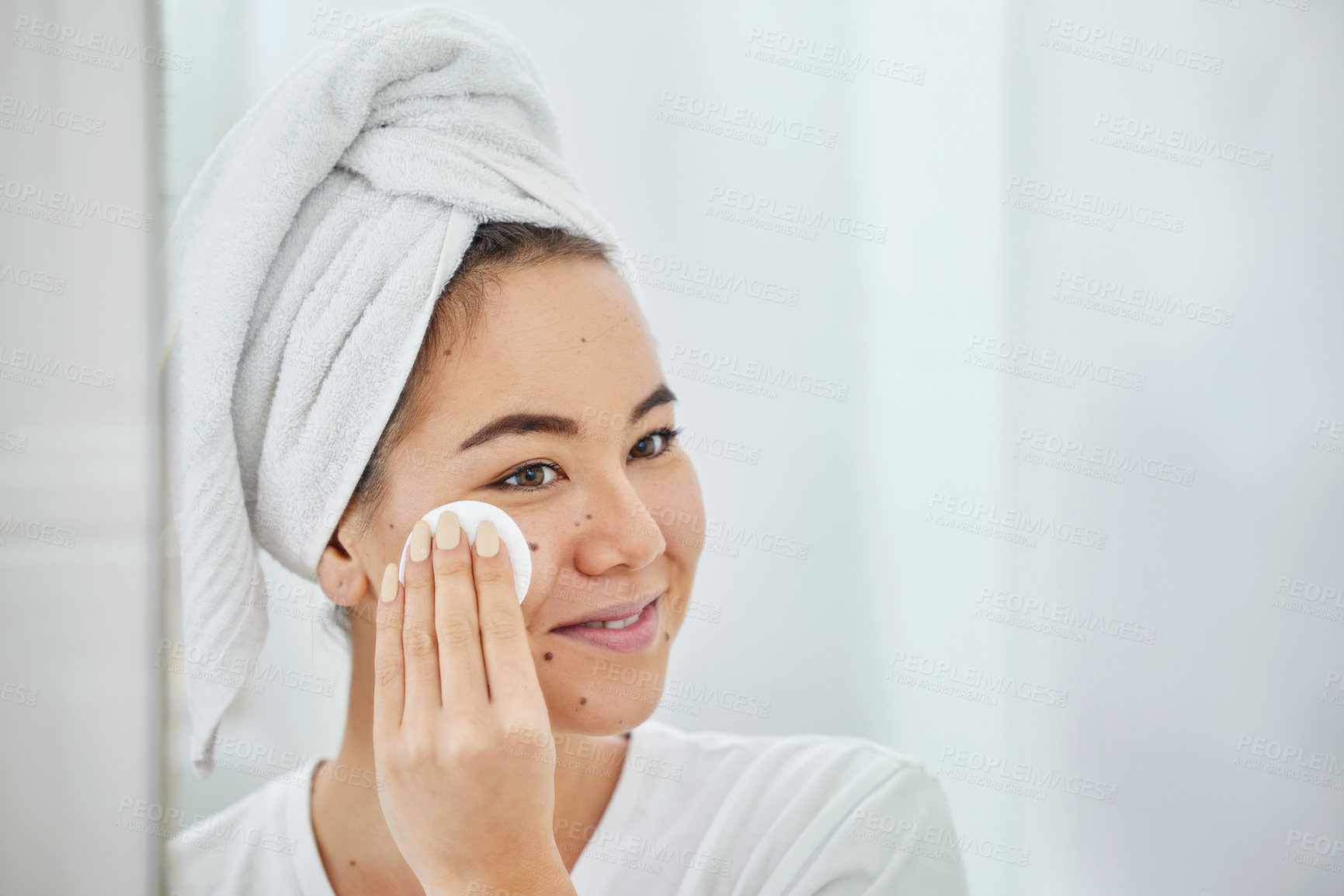 Buy stock photo Shot of a young woman cleaning her face with a cotton pad in a bathroom at home