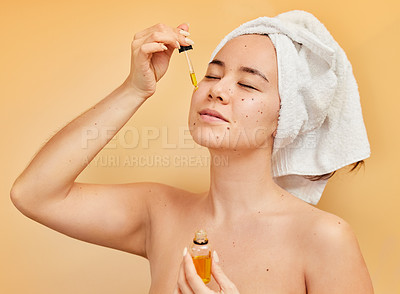 Buy stock photo Shot of a young woman applying a serum to her face during her morning beauty routine against a yellow background