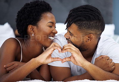 Buy stock photo Shot of a young couple making a heart shaped gesture in bed at home